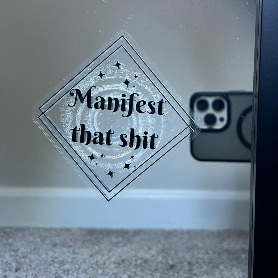 Vinyl decal stuck onto a mirror with the design double black squares with black stars and gold sprinkle dust black text that read Manifest that shit