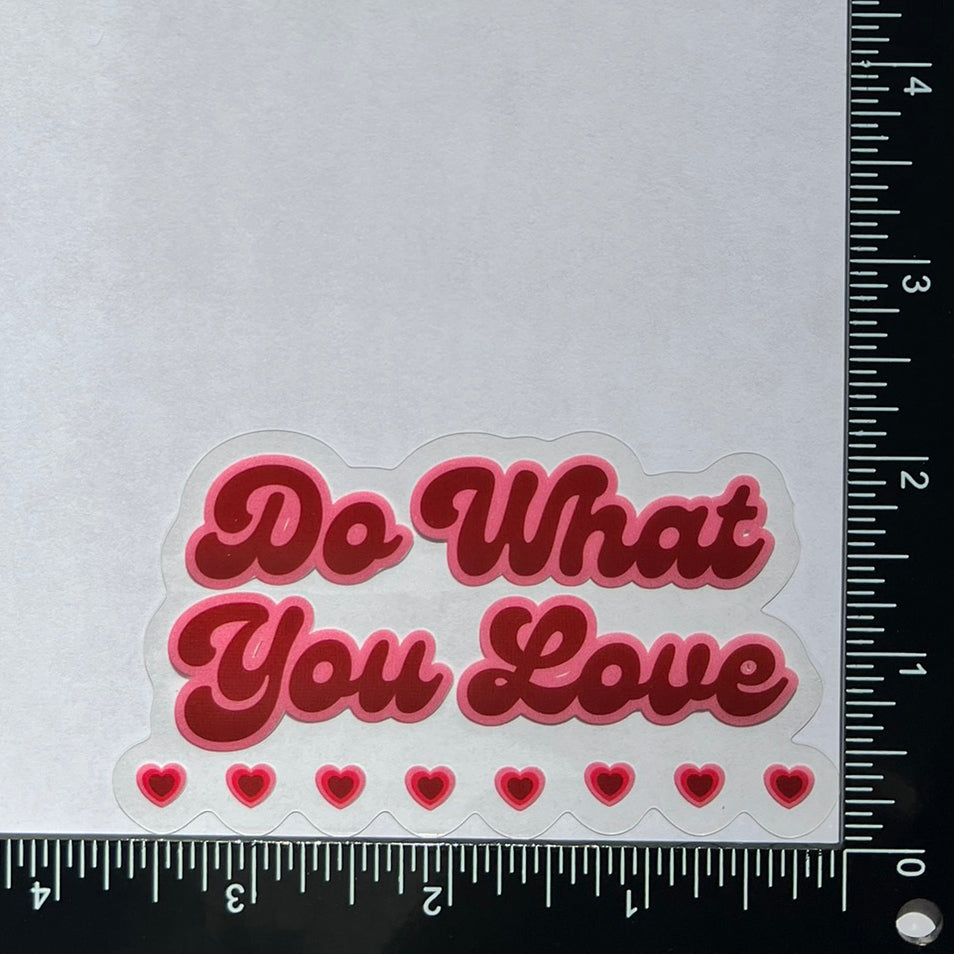 Window and mirror cling reusable sticker with phrase "Do What You Love" in red cursive font with pink outline and eight little hearts on the bottom measuring 3.75 inches wide by 2.25 inches tall